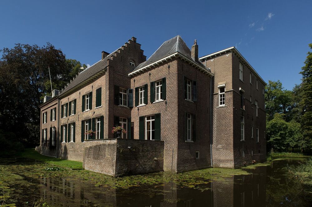 Kasteel Geldrop gezien over de slotgracht, met trapgevel en luiken onder een strakblauwe lucht